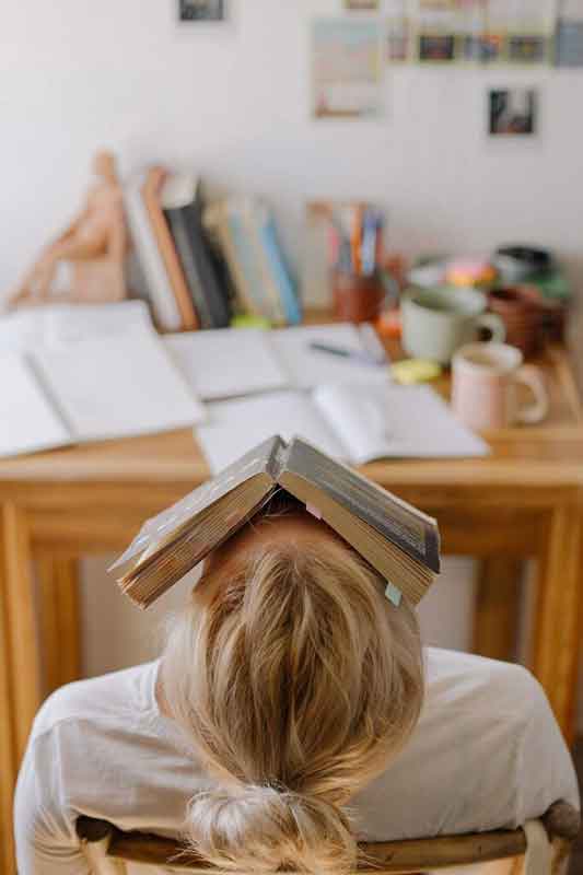 estudiar mejor, aumentar rendimiento mental, mujer estresada con un libro en la cara porque trata de memorizar de forma literal sin comprender lo que estudia, y le gustaría aprender más rápido